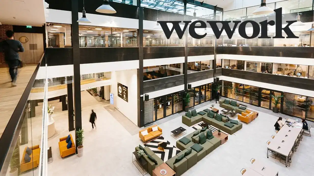 Multi-level WeWork atrium with lounge seating, glass offices, and the WeWork logo visible on an upper floor